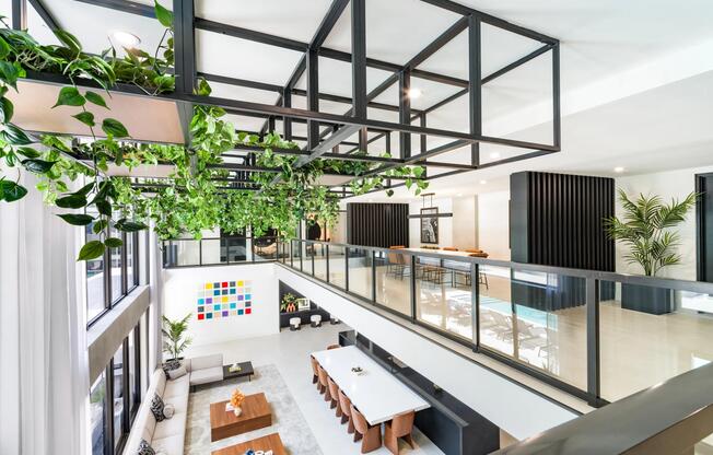 Multi-level resident lounge with hanging greenery, communal tables, and open sightlines that connect gathering spaces across both floors.
