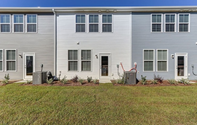North Charleston, SC Townhomes Near The Citadel - Highland Townhomes - Exterior View of Townhomes with White and Grey Walls, and Backyards with Manicured Grass Lawns.