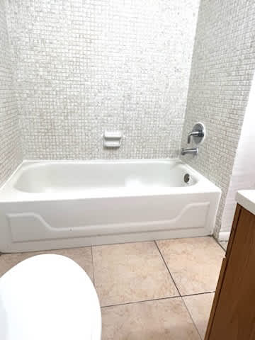 A white bathtub in a bathroom with a white toilet and a tiled wall.