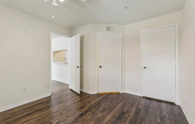 A room with white walls and wood flooring with three doors.