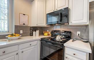 A black microwave is mounted above a black stove in a kitchen with white cabinets.at Palazzo Townhomes, Phoenix