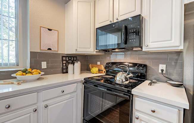 A black microwave is mounted above a black stove in a kitchen with white cabinets.at Palazzo Townhomes, Phoenix  