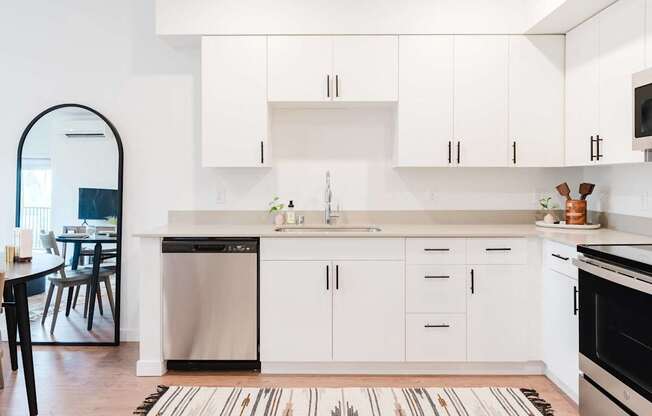 A modern kitchen with white cabinets and a striped rug on the floor.