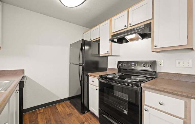 A kitchen with black and white appliances and vinyl wood grain floors at Clackamas Trails Apartments, Oregon, 97222