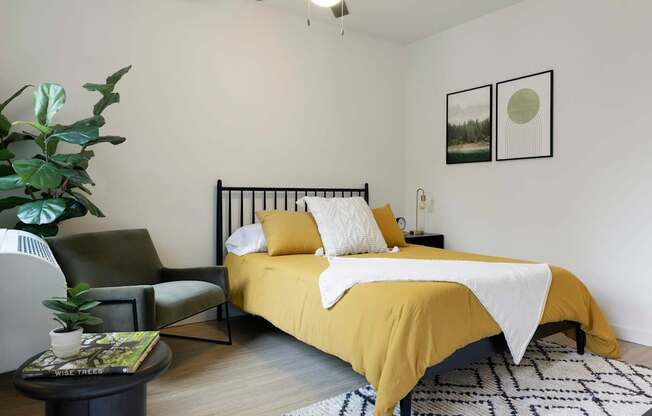 A bedroom with a bed, chair, and potted plant.