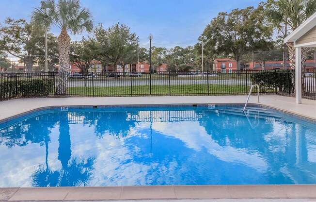 A swimming pool surrounded by a black fence with trees in the background.