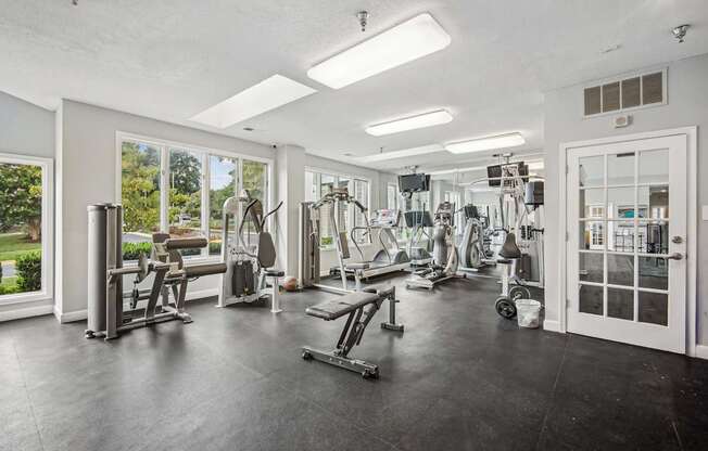 A spacious gym with a variety of equipment and a view of the outdoors through the windows.