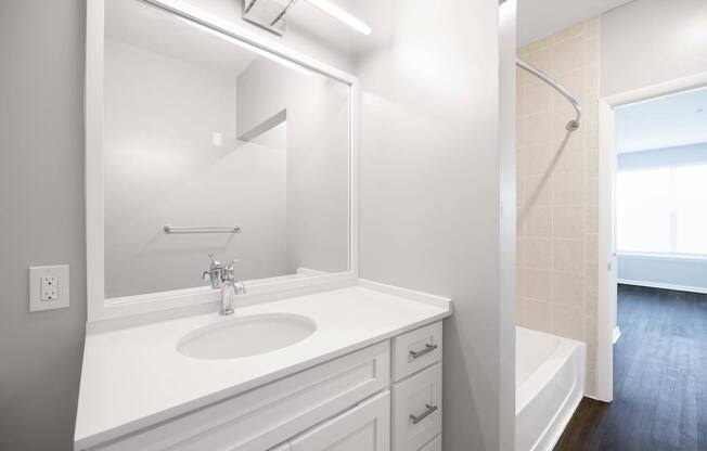 A white bathroom with a sink, mirror, and bathtub.