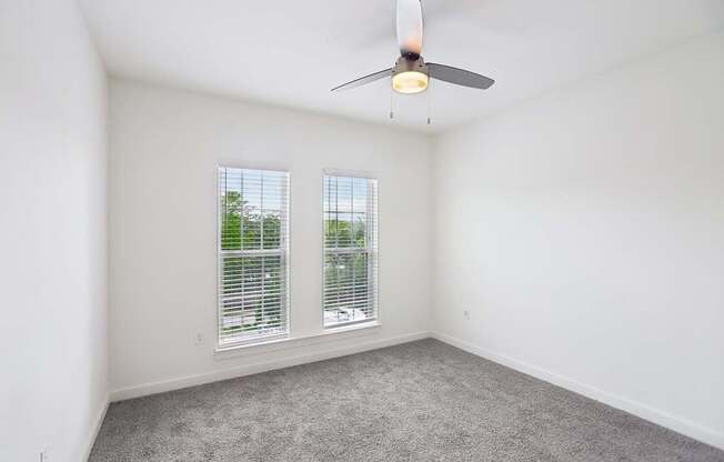 A bedroom with a ceiling fan and two windows.