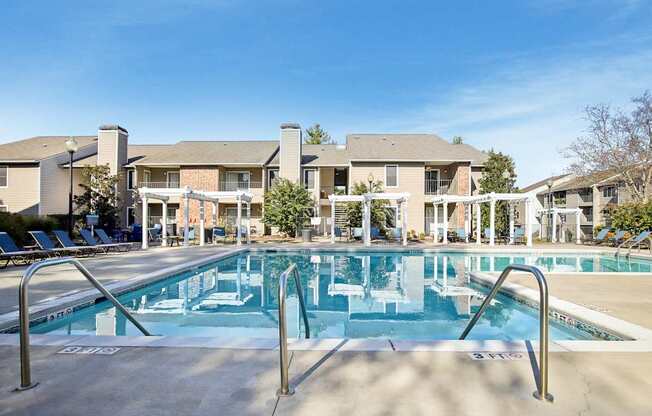 A large swimming pool in front of a building with lounge chairs around it.