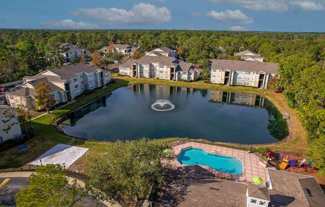 A large swimming pool surrounded by a fence and a small lake in the middle of a housing complex.