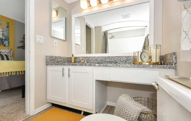 Model apartment bathroom with granite countertops, a large mirror, and ample lighting at The Oasis Daytona