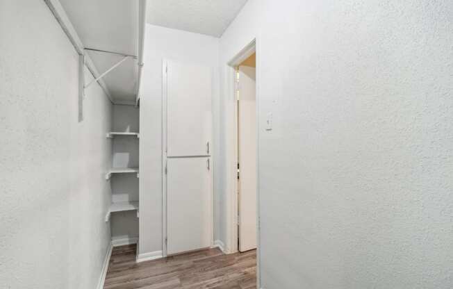 a walk-in closet with white walls and hardwood floors