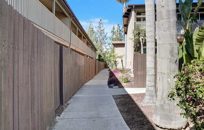 A concrete pathway leads to a building with a brown fence on the left.