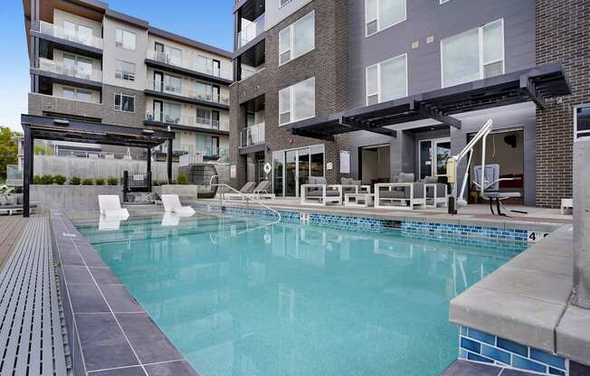 A swimming pool in a residential area with a deck and lounge chairs.