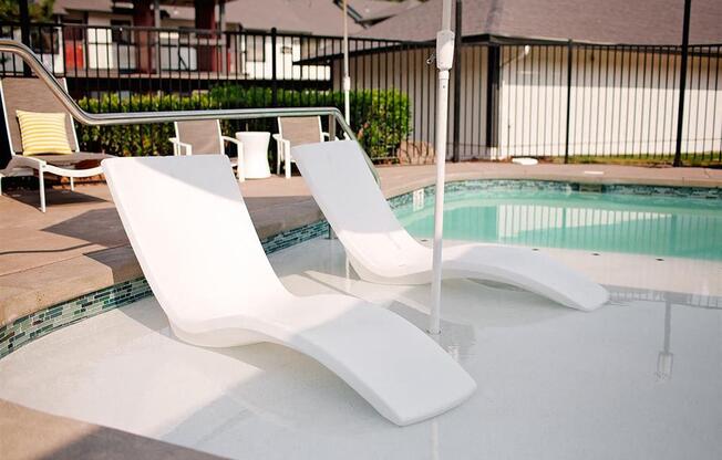 Two white chairs are placed by a pool.