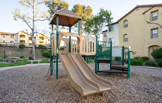 A playground with a slide and a green fence.