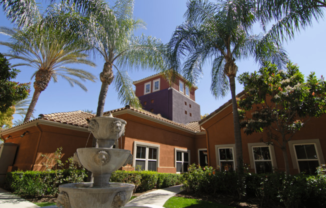 A fountain in front of a house with palm trees.