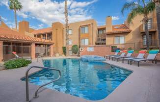 A pool surrounded by sun loungers and palm trees.