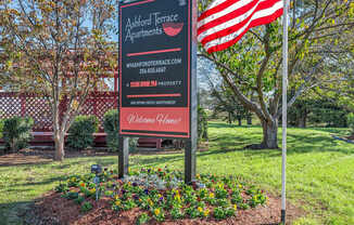 A sign for Ackford Terrace Apartments is in front of a tree and an American flag.