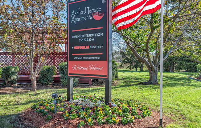 A sign for Ackford Terrace Apartments is in front of a tree and an American flag.
