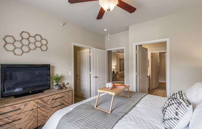 A bedroom with a bed, a television, and a ceiling fan.