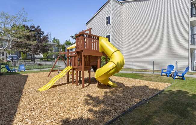 Property Playground with a yellow slide and a wooden deck with blue chairs in an outdoor area at Park Edmonds Apartment Homes, Edmonds, Washington