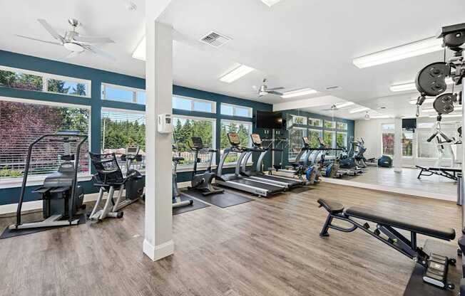 A gym with a variety of equipment including treadmills, weights, and a bench at The Madison apartments in Olympia, WA