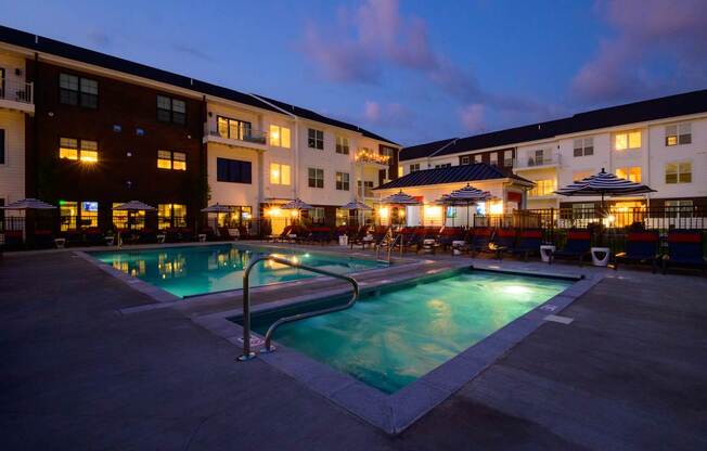 A swimming pool in front of a building with lights on.