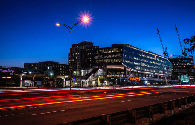 A view of Boston Landing lit up at night with cranes in the background and the Mass Pike in the foreground