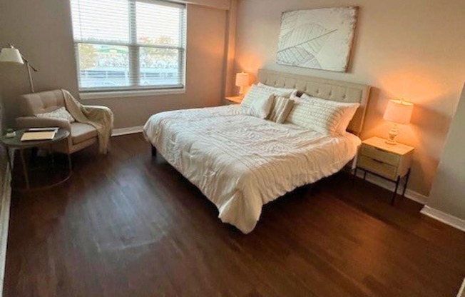 A bedroom with a large bed, a chair, and a window.