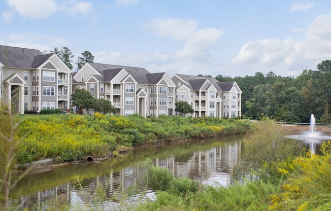 Gorgeous apartment community surrounded by lush landscaping and scenic pond on a sunny day
