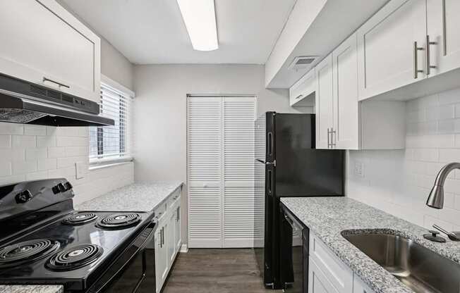 A black refrigerator stands in a kitchen with white cabinets and a black stove.