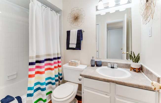 a bathroom with a white sink and toilet next to a shower curtain with a rainbow striped shower