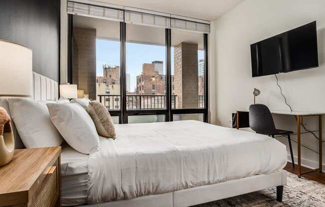 A bedroom with a large bed, a chair, and a flat-screen TV mounted on the wall.