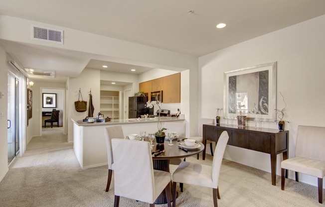 a dining area with a table and chairs and a kitchen in the background