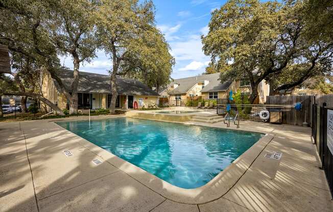 A small pool surrounded by a concrete patio and trees.