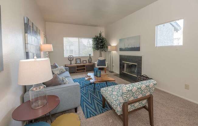A living room with a grey couch, a blue and white patterned chair, a fireplace, and a painting on the wall at Autumn Oaks Apartments, Roseville, CA, 95678