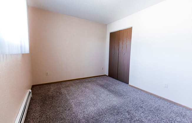 Grand Forks, ND Cherry Creek Apartments. A bedroom with a closet, window, white walls, and carpeted floors