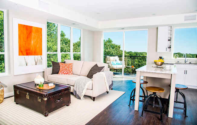 An elegant living room with luxurious stain-resistant plank flooring, a gas fireplace, and expansive windows that offer picturesque views of nature. A seamless transition to a balcony creates a spacious indoor-outdoor connection.