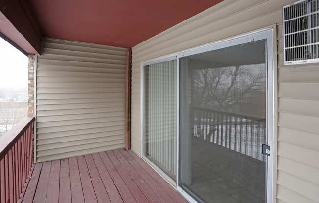 Outdoor private balcony with wood railing and sliding glass door leading inside