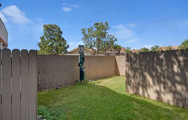 A fenced pet relief area here at Summertree Place featuring a grassy enclosed space with wooden privacy fencing, a convenient waste station, and open sky overhead, providing a clean and practical outdoor area for residents to enjoy time with their pets.