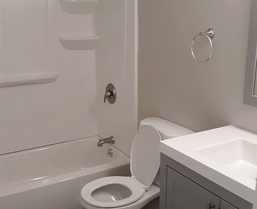 View of renovated bathroom showing soaking tub, toilet, and sink with grey cabinets