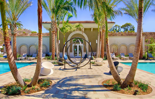 A poolside area with palm trees and a large circular sculpture.