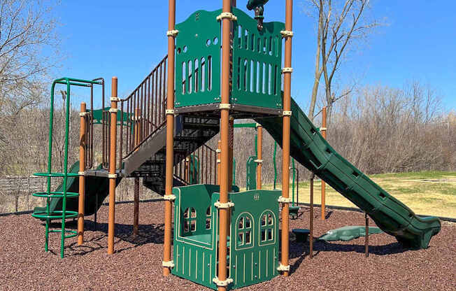 A playground with a green slide and a wooden structure.