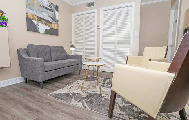 A grey couch sits in a leasing office with a small table and a chair at The Creole Apartments in Shreveport, LA