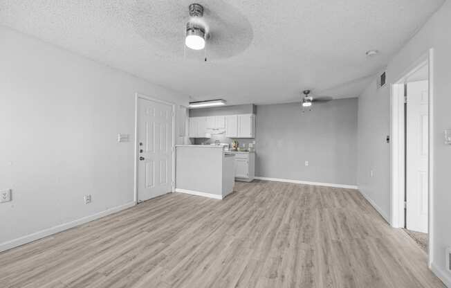 the living room and kitchen of an apartment with white walls and wood flooring