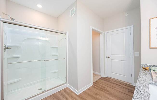 A white bathroom with a walk-in shower and a white door.