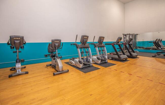 A gym with exercise equipment and wooden floors.