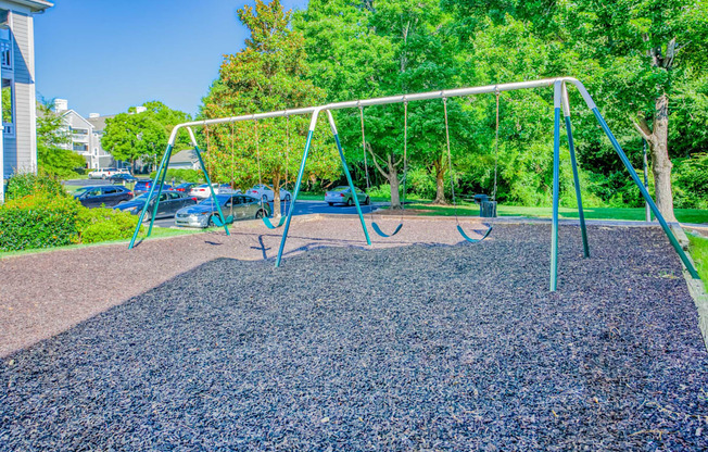 A playground with a swing set in the middle of a gravel area.